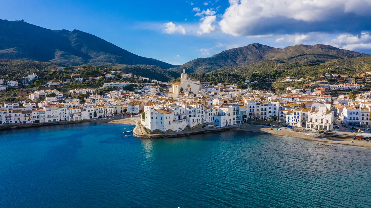 The whitewashed seaside town of Cadaqués on the Costa Brava, curving around a deep blue Mediterranean bay with hills behind